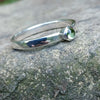 A sterling silver ring with a round, bezel-set green Peridot gemstone, photographed close-up against a textured gray stone background.