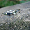 A sterling silver ring with a round, bezel-set green Peridot gemstone, photographed close-up against a textured gray stone background.