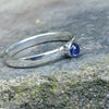 A sterling silver ring with a round, bezel-set watery blue Iolite gemstone, photographed close-up against a textured gray stone background.