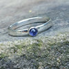 A sterling silver ring with a round, bezel-set watery blue Iolite gemstone, photographed close-up against a textured gray stone background.