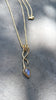 9ct yellow gold tendril pendant with a bezel set  bud shaped Labradorite stone on a substantial gold chain. The gold tendril loops around the chain twice and curve back down to a point. taken against a slate background.