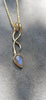 9ct yellow gold tendril pendant with a bezel set  bud shaped Labradorite stone on a substantial gold chain. The gold tendril loops around the chain twice and curve back down to a point. taken against a slate background.