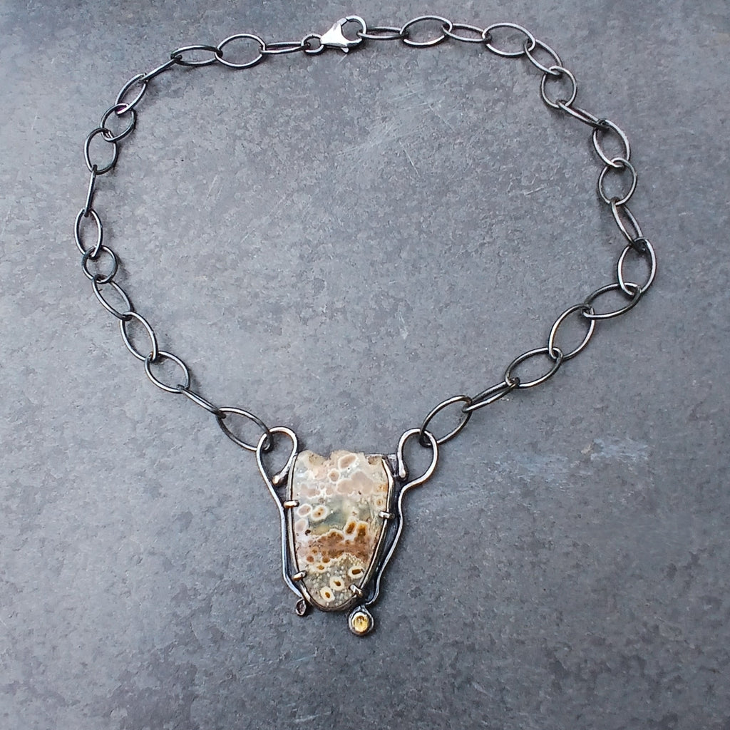 An oxidised sterling silver chain necklace with a shield-shaped natural edge ocean jasper pendant and a small round citrine stone, displayed on a slate surface.