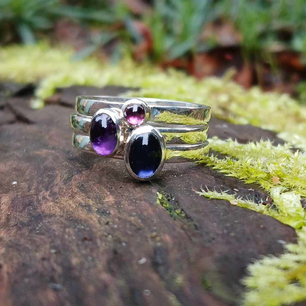 Silver 3 ring stacking set Amethyst oval Iolite oval and Garnet round. sitting on a mossy log