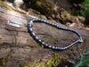 Long slim blue green seaglass pendant on black freshwater pearls lying on a mossy woodland log.