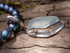 Long slim blue green seaglass pendant on black freshwater pearls lying on a mossy woodland log. Close up side view.