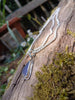 Triangle-ish  deep blue seaglass pendant with tendril detail on thick spiga chain on a mossy wooodland log.