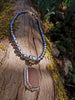 Large rusty orange seaglass pendant with tendril detail on black rice shaped pearl beads draped on a mossy woodland log.