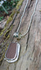 Large rusty orange seaglass pendant with tendril detail on smooth slim snake chain draped on a mossy woodland log.