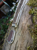 Large rusty orange seaglass pendant with tendril detail on thick spiga chain draped on a mossy woodland log.