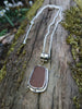 Large rusty orange seaglass pendant with tendril detail on thick spiga chain draped on a mossy woodland log.