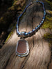 Large rusty orange seaglass pendant with tendril detail on black rice shaped pearl beads draped on a mossy woodland log.