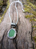 Bright green seaglass pendant with tendril detail on thick spiga chain draped on a mossy woodland log.