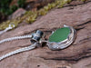 Bright green seaglass pendant with tendril detail on thick spiga chain draped on a mossy woodland log.