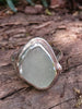 Pale blueish green seaglass ring with slightly egg shaped stone and tendril detail wrapping around, sitting on a mossy log.