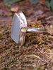 Large Palest blue seaglass ring with  and tendril detail wrapping around, sitting on a mossy log. Roughly diamond shaped.