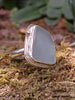 Large Palest blue seaglass ring with  and tendril detail wrapping around, sitting on a mossy log. Roughly diamond shaped.