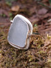 Large Palest blue seaglass ring with  and tendril detail wrapping around, sitting on a mossy log. Roughly diamond shaped.