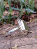 Sterling silver ring with an acidic green triangle sea glass and winding tendril sits on a mossy log in the sunshine. Side view