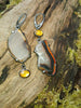Mismatched dangle earrings with agate slices set with prongs and bezel set amber, lying on a mossy log in the sunshine.