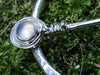 Close up of the hilt of the pin set with an opalite stone with a wrapped detail. Traditional Silver brooch, penannular pin, ring pin with blue stones on a bed of green moss. 