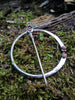 Traditional Silver brooch, penannular pin, ring pin with red and pink stones sits on a mossy log.