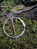 Traditional Silver brooch, penannular pin, ring pin with red and pink stones sits on a mossy log.