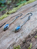 Labradorite leaf and long stem earrings with hook wires sitting on a mossy log, the labradorite stone glinting blue in the sunlight.