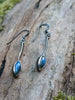 Labradorite leaf and long stem earrings with hook wires sitting on a mossy log, the labradorite stone glinting blue in the sunlight.