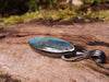 Large oval Labradorite and oxidised sterling silver pendant on it's own, with no chain sitting on a mossy log, the labradorite stone bud is clasped by black tendrils  and glints blue in the sunlight.