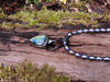 Labradorite bud and oxidised sterling silver pendant on a strand of lustrous black pearl beads sitting on a mossy log, glinting blue in the sunlight.