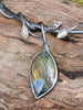 Close up showing large leaf shaped stone and three smaller winding leaves. An oxidised silver necklace with a dreamy elfin quality sits on a mossy log in the sunlight.