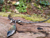 An oxidised silver necklace with a dreamy elfin quality sits on a mossy log in the sunlight.