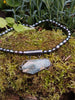 Oxidised silver pendant with coffin shaped  moss agate stone on black oval shaped freshwater pearl beads. Sitting on a mossy log 