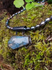 Oxidised silver pendant with coffin shaped  moss agate stone on black oval shaped freshwater pearl beads. Sitting on a mossy log 