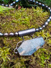 Oxidised silver pendant with coffin shaped  moss agate stone on black oval shaped freshwater pearl beads. Sitting on a mossy log 