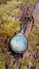 Oxidised silver pendant with a fat teardrop Labradorite stone and a chunky chain sitting on a mossy log.