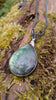 Oxidised silver pendant with a fat teardrop Labradorite stone and a chunky chain sitting on a mossy log.