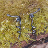 oxidised black Sterling silver twisted tendril studs sit on a mossy log