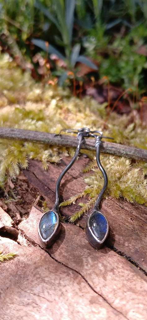 a pair of oxidised silver dangly earrings with leaf shaped blue flash labradorite on a mossy log