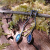 a pair of oxidised silver dangly earrings with leaf shaped blue flash labradorite on a mossy log