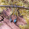 a pair of oxidised silver dangly earrings with bud shaped blue flash labradorite on a mossy log