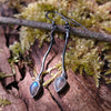a pair of oxidised silver dangly earrings with bud shaped blue flash labradorite on a mossy log