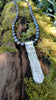 Medium Straight sterling silver melt textured pendant on black freshwater pearl beads. the necklace lies on a mossy woodland log.