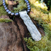 Medium Straight sterling silver melt textured pendant on black freshwater pearl beads. the necklace lies on a mossy woodland log.