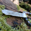 Medium Straight sterling silver melt textured pendant on black freshwater pearl beads. the necklace lies on a mossy woodland log.