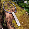 Long Straight sterling silver melt textured pendant on black freshwater pearl beads. the necklace lies on a mossy woodland log.