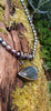 Oxidised black silver tendril pendant with blue flash labradorite bud winds around black oval freshwater pearls. Pictured on a mossy log. 