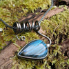 Oxidised black silver tendril pendant with blue flash labradorite bud winds around a chunky blackened silver spiga chain. Pictured on a mossy log