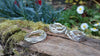 three wibbly wobbly molten textured silver rings sit on a mossy log with daisys in the backround.